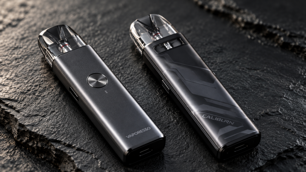 A precise studio macro photograph comparing the Vaporesso XROS 4 (gunmetal) and Uwell Caliburn G3 (space grey) pod systems side-by-side on a dark slate surface, highlighting the physical fire button on the XROS 4.