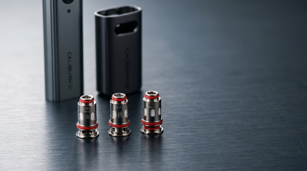 Caliburn G vs G2 coil -- three resistance options 0.8ohm 1.0ohm and 1.2ohm laid on deep slate surface beside Caliburn G and G2 pod devices